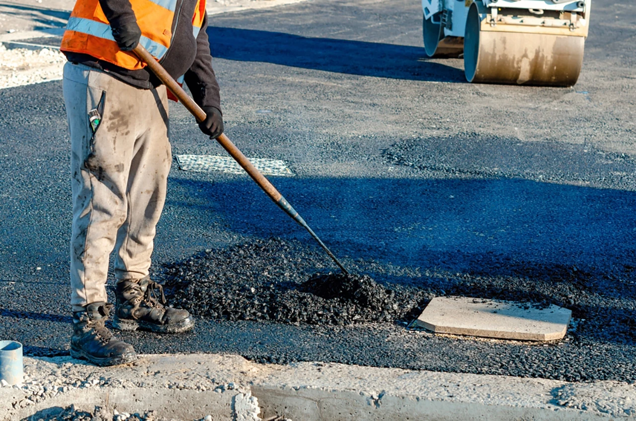 Pothole in asphalt being repaired with hot mix asphalt and compaction
